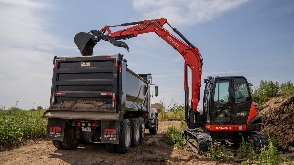 Kubota excavator loading soil and debris into a dump truck during site cleanup and haul-away