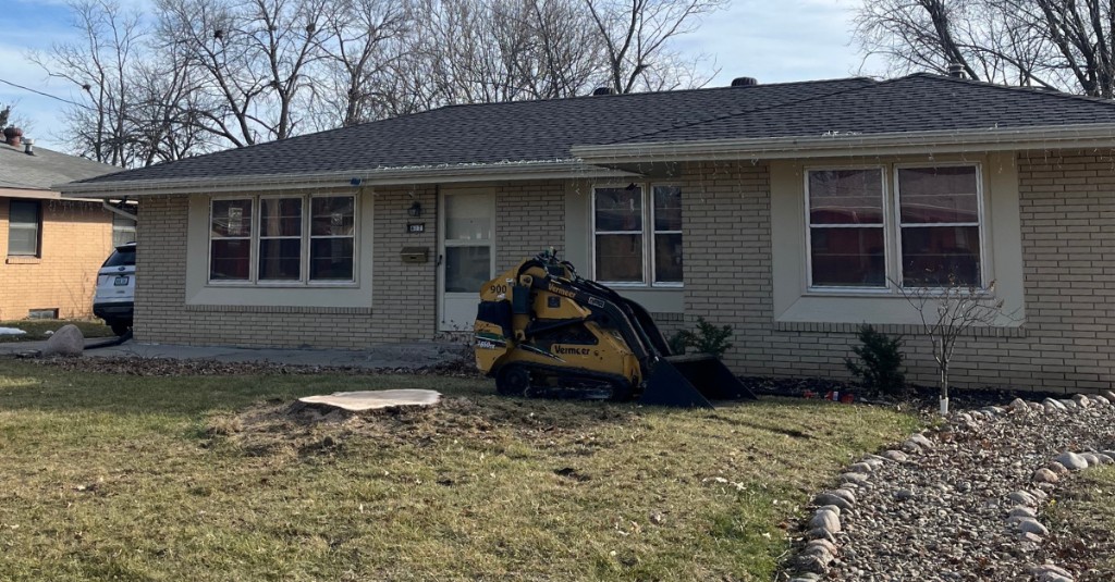 Vermeer mini skid steer on a residential lawn next to a freshly cut tree stump after tree removal